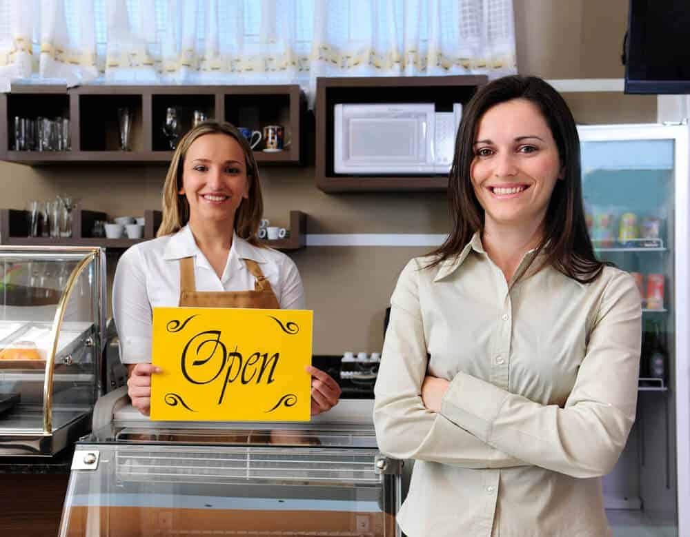 A Commercial Realtor next to a store owner holding an open for business sign.