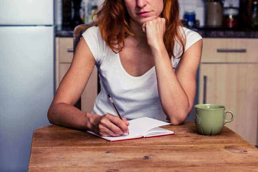 A woman at the kitchen table making a list on note paper