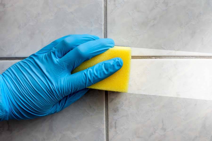 A gloved hand cleaning tile with a sponge.