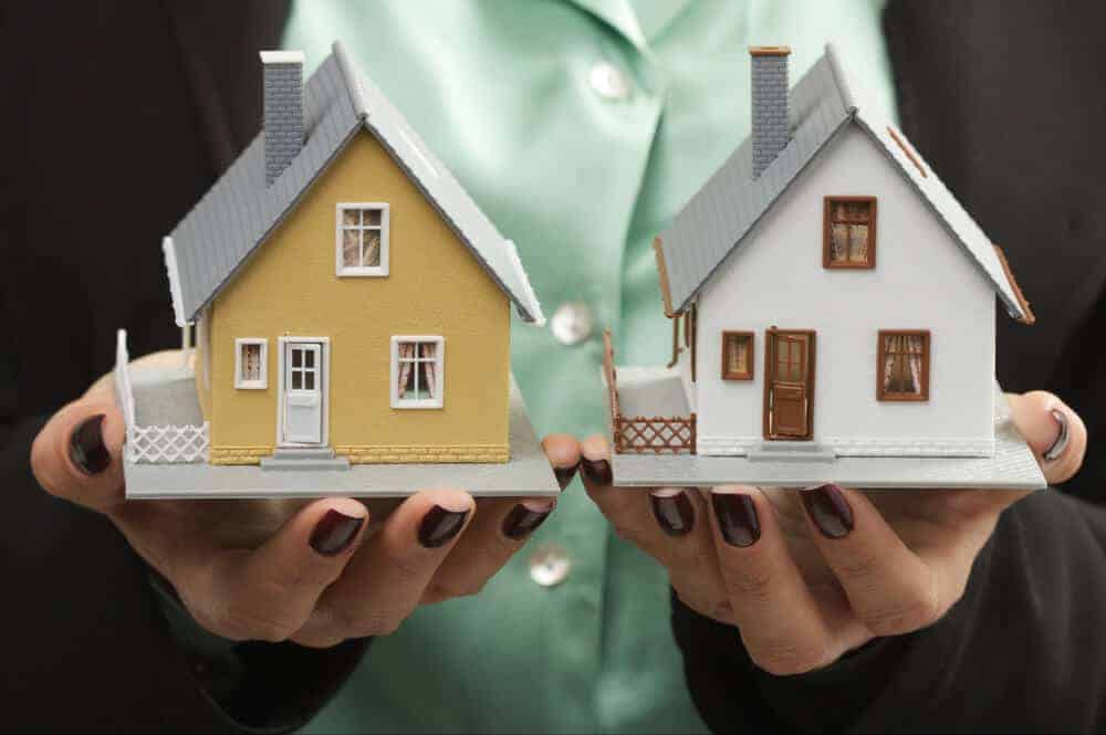 two hands holding models of two homes concept of buying and selling real estate at the same time