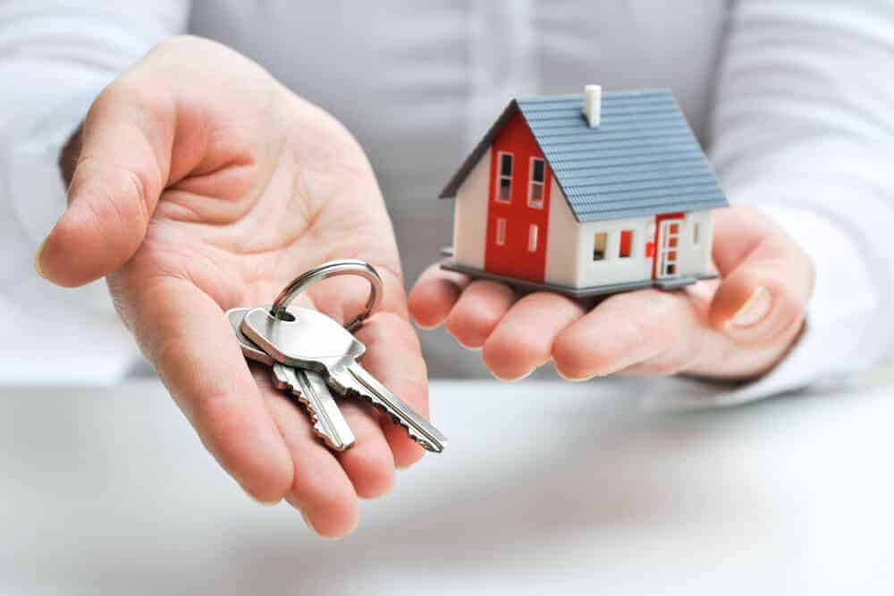 hands holding house keys and a toy model of a home, concept representing Becoming a realtor