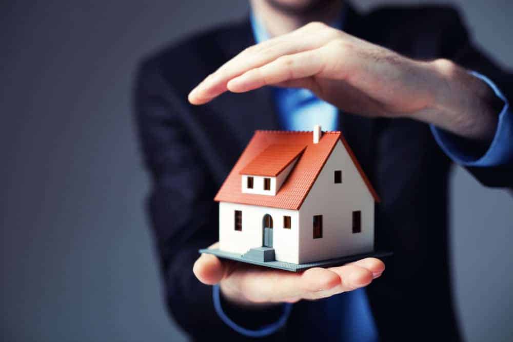 Man holding a toy model of a house and protecting it with his hand, Home Insurance