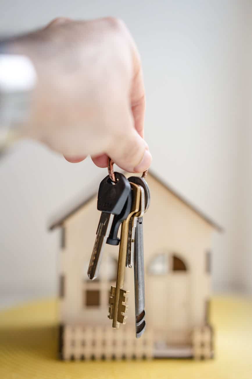 hand holding keys in front of a model home