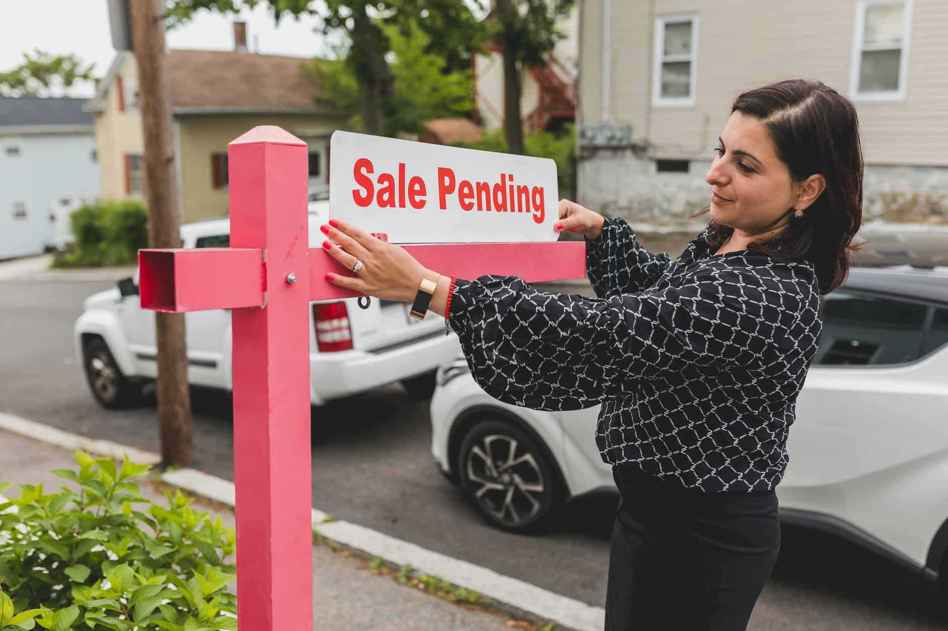 Woman placing a sale pending sign on a sign post with two cars behind her